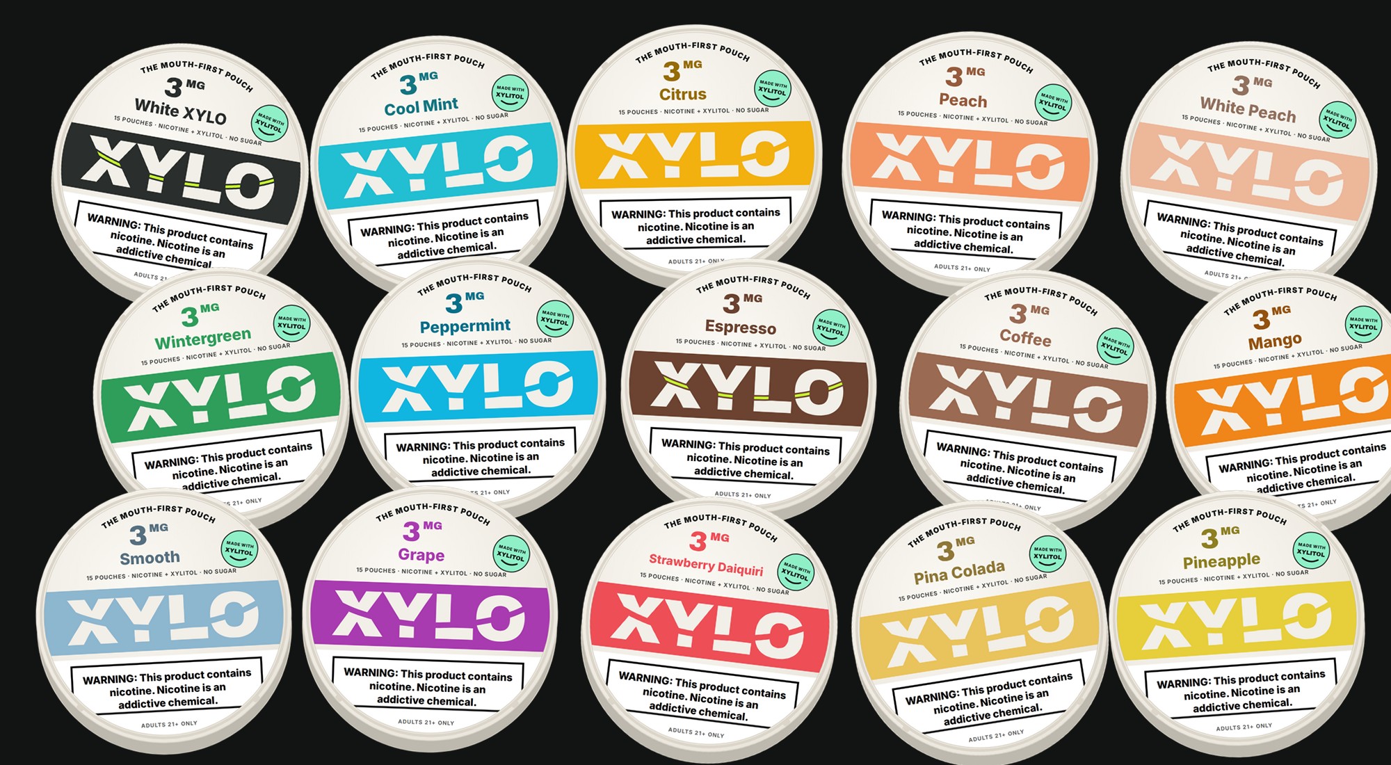 All fifteen revamped XYLO cans on charcoal: White XYLO, Cool Mint, Citrus, Peach, White Peach, Wintergreen, Peppermint, Espresso, Coffee, Mango, Smooth, Grape, Strawberry Daiquiri, Pina Colada and Pineapple